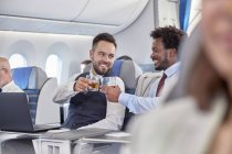Empresarios brindando vasos de whisky en primera clase en avión - foto de stock
