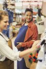 Cajero ayudando a las mujeres embarazadas compradoras en la caja registradora de la tienda de comestibles - foto de stock