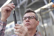 Supervisor masculino focado examinando cabo de fibra óptica na fábrica — Fotografia de Stock
