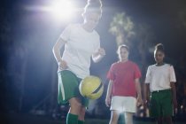 Focused young female soccer player practicing on field at night, kneeing the ball — Stock Photo