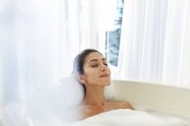 Mujer serena disfrutando de baño de burbujas con los ojos cerrados - foto de stock