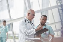 Male doctor and nurse with clipboard talking in hospital lobby — Stock Photo