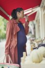 Pregnant woman shopping, smelling fruit at market storefront — Stock Photo