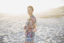 Retrato sonriente, mujer morena confiada en traje de baño encubierta en la soleada playa del atardecer de verano - foto de stock