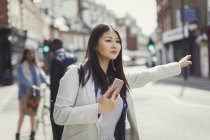 Молода бізнес-леді з мобільним телефоном вимотує таксі на сонячній міській вулиці — стокове фото