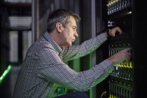 Técnico de TI masculino focado trabalhando no painel na sala escura do servidor — Fotografia de Stock