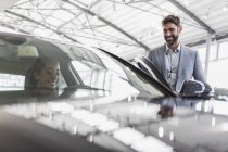 Smiling car salesman and female customer in driver?s seat of new car in car dealership showroom — Stock Photo