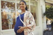 Retrato sonriente mujer embarazada fuera escaparate - foto de stock
