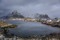 Fishing village at waterfront below snowy, rugged mountains, Reine, Lofoten, Norway — Stock Photo
