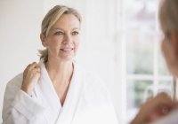 Lächelnde reife Frau im Bademantel am Badezimmerspiegel — Stockfoto
