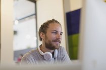 Homme d'affaires créatif confiant avec écouteurs travaillant à l'ordinateur — Photo de stock