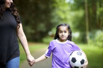 Portrait girl with soccer ball holding hands with mother — Stock Photo