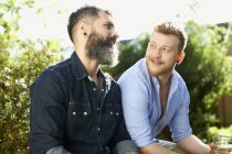 Мужская гей-пара разговаривает в саду — стоковое фото