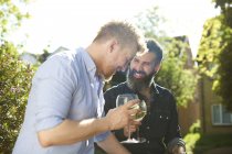 Счастливая гей-пара пьет вино в солнечном саду — стоковое фото
