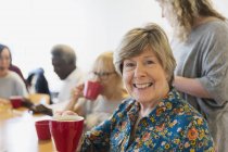 Портрет улыбающейся, уверенной пожилой женщины, пьющей чай с друзьями в общественном центре — стоковое фото
