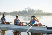 Female rowing team resting, drinking water in scull on sunny lake — Stock Photo