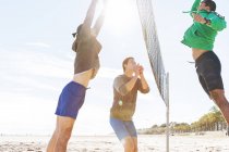 Uomini che giocano a beach volley sulla spiaggia soleggiata — Foto stock