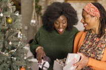 Mother surprising daughter with gift next to Christmas tree — Stock Photo