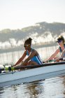 Female rowing team rowing scull on sunny lake — Stock Photo