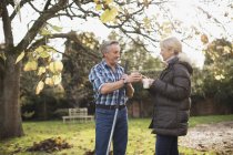 Mature caucasian couple with rakes drinking coffee at garden — Stock Photo