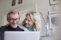 Souriant couple d'âge mûr en utilisant un ordinateur portable à la maison moderne — Photo de stock
