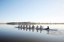 Female rowing team rowing scull on tranquil lake — Stock Photo