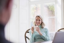 Улыбающаяся взрослая женщина пьет чай, разговаривает с мужчиной — стоковое фото