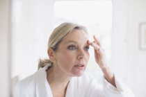 Ältere Frau berührt Augenbraue im Badezimmerspiegel — Stockfoto