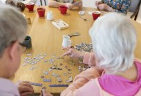 Senior friends assembling jigsaw puzzle at table in community center — Stock Photo
