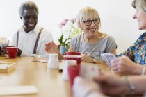 Happy senior friends playing cards at tale in community center — Stock Photo