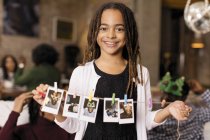 Ritratto sorridente ragazza tenendo stringa di foto istantanee — Foto stock