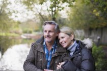 Mature caucasian couple standing by fence together in autumn park — Stock Photo