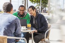 Чоловіки друзі використовують ноутбук у сонячному тротуарному кафе — стокове фото