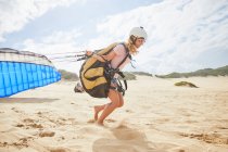 Женщина-параплан, бегущая с парашютом на солнечном пляже — стоковое фото