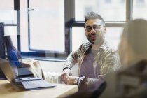 Empresário sorridente em laptop conversando com colega em reunião de escritório — Fotografia de Stock