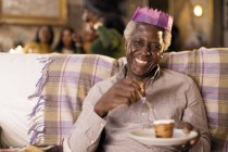 Portrait smiling, happy senior man wearing Christmas paper crown, enjoying dessert — Stock Photo