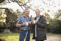 Mature caucasian couple with rakes drinking coffee at garden — Stock Photo