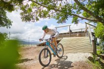 Focused man mountain biking down sunny obstacle course ramp — Stock Photo