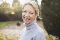 Portrait of happy blond woman in grey sweater at garden — Stock Photo