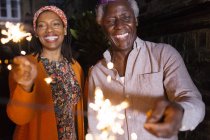 Portrait happy senior father and daughter celebrating with sparklers — Stock Photo