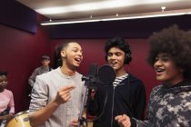 Des musiciens adolescents souriants enregistrant de la musique, chantant dans une cabine sonore — Photo de stock