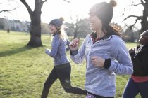 Усміхнені жінки бігають у сонячному парку — стокове фото