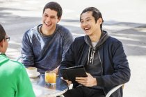Мужчины с цифровыми планшетами смеются в кафе на тротуаре — стоковое фото