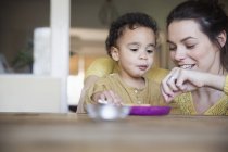Happy caucasian mother feeding little african american son — Stock Photo