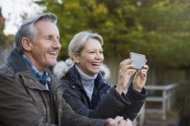 Mature caucasian couple taking photo on smartphone at autumn park — Stock Photo