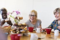 Amigos seniores desfrutando de chá da tarde e sobremesa no centro comunitário — Fotografia de Stock