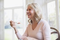 Счастливая зрелая женщина ест фрукты в современном доме — стоковое фото