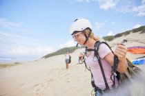 Parapendio femminile sorridente con attrezzatura sulla spiaggia — Foto stock