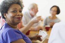Retrato confiado mujer mayor jugando a las cartas con amigos en el centro comunitario - foto de stock