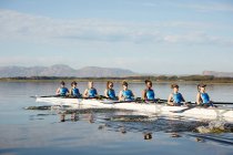Female rowing team rowing scull on sunny lake — Stock Photo